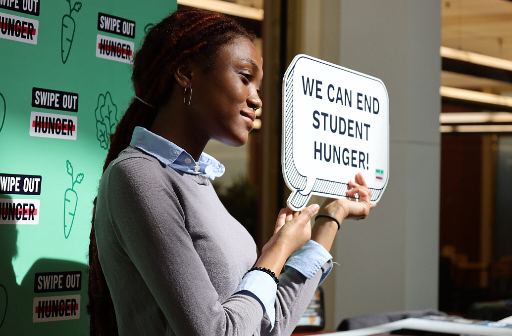 student holding a sign that says "we can end student hunger"